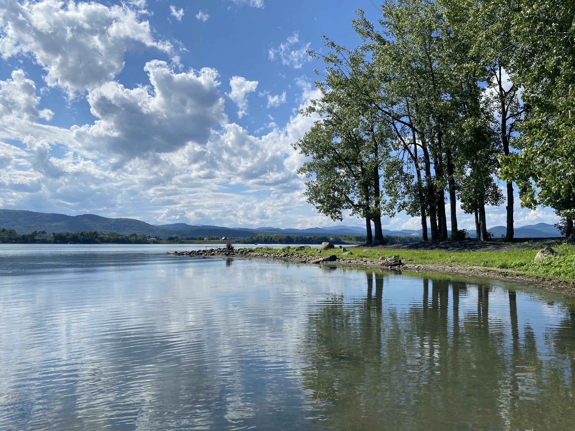 Lake Champlain shoreline near the Whitford House on a bright day with blue sky and clouds.